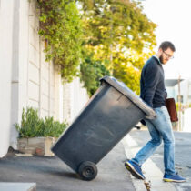 Man pulling a wheeled dumpster out of his garage while going to work